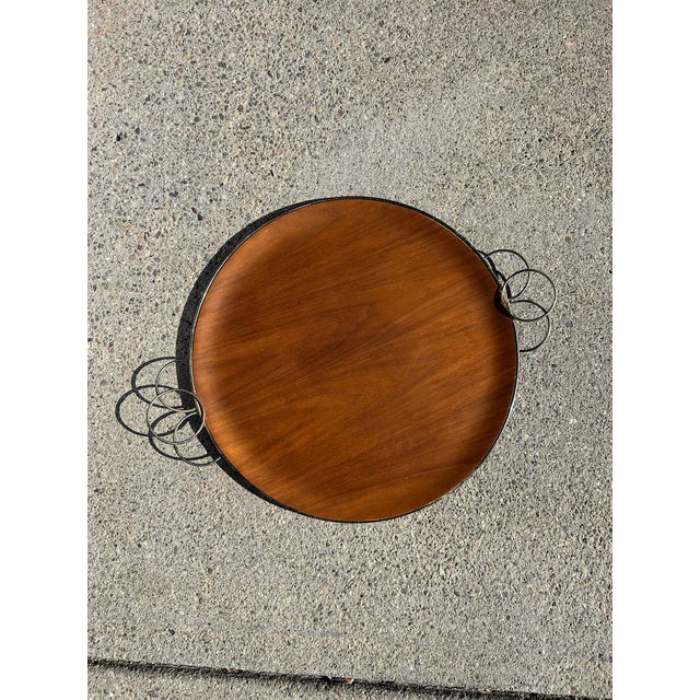 Vintage mid-century round serving tray featuring a warm-toned wood surface framed by a slim metal surround. The tray is...