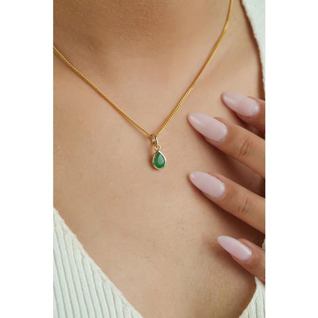 This elegant pendant showcases a 0.66 carat natural zambian pear-cut emerald, set in 14k yellow gold. The emerald...