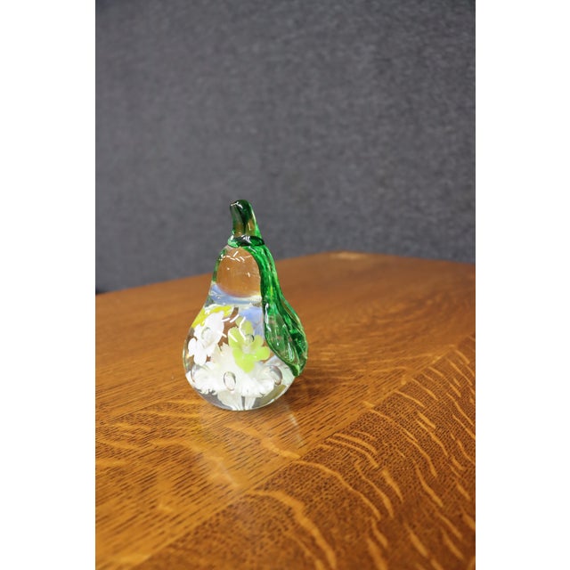 Handcrafted art glass paperweight in the form of a pear with an applied green leaf and stem. The clear glass body encloses...