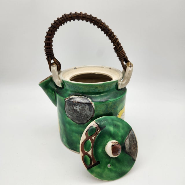 Japanese green-glazed ceramic teapot with hand-painted floral motifs and woven rattan handle