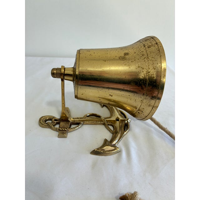 A vintage solid brass bell set on a cast anchor bracket with rope detailing, with a braided cotton pull rope. The bracket...