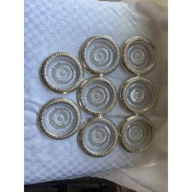 A set of 8 sterling silver rimmed coasters. The sterling silver rims are a floral repousse pattern over a pressed glass...