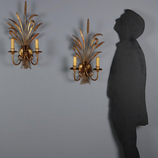 A pair of wrought iron, pastiglia, and wood wall sconces, crafted and gilded. Two lights supported by curled arms rest on...