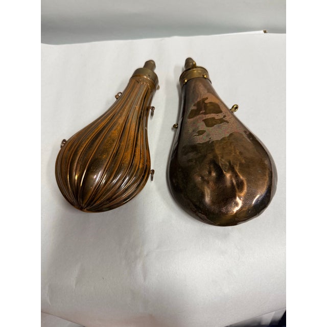 Two copper powder flasks from the 19th century. One is signed American Flask and Cap Co. The other has no signature but is...