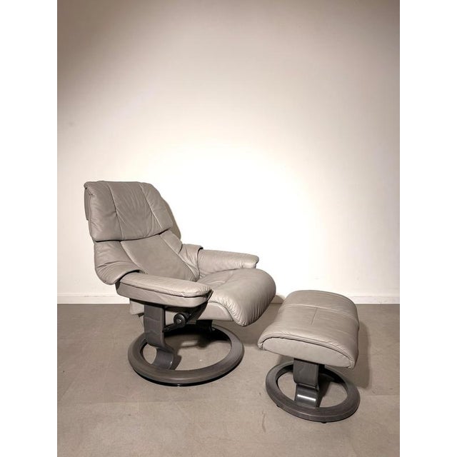 Comfortable Stressless recliner with matching footstool , upholstered in soft light grey leather and set on the brand’s...