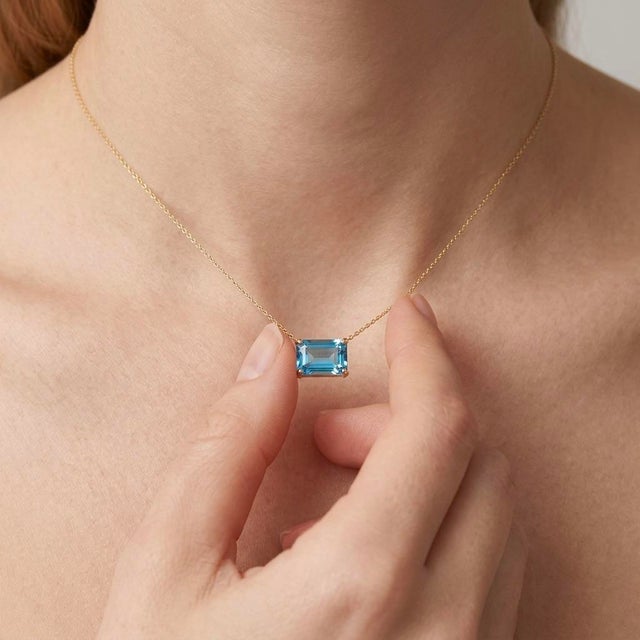 Capture the serene elegance of clear blue skies with this modern East-West Emerald Cut Blue Topaz Necklace. This design...