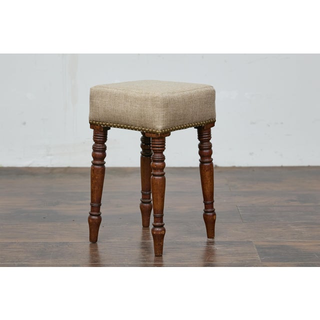 An English petite wooden stool from the 19th century with diamond top, turned legs and custom linen fabric. This petite...