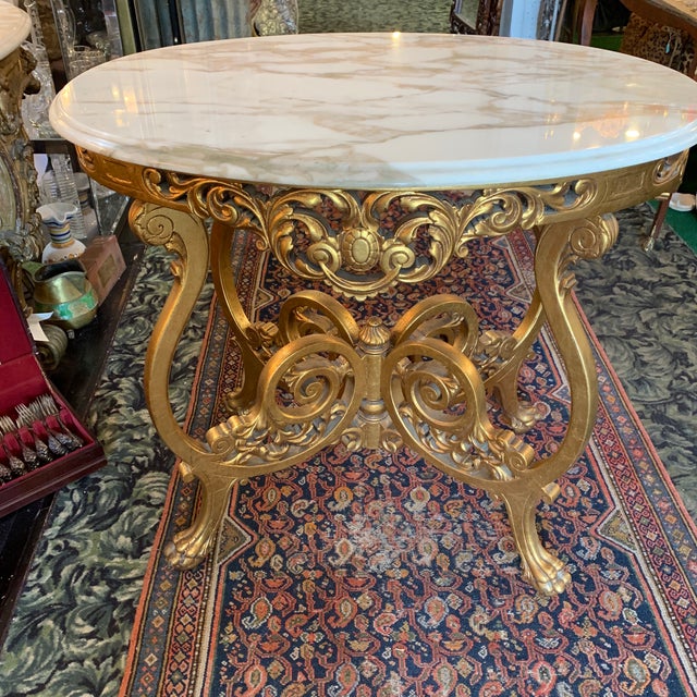 A Rococo style carved and gilded wood console table with large marble top with scroll legs on paw feet. Gold leaf...