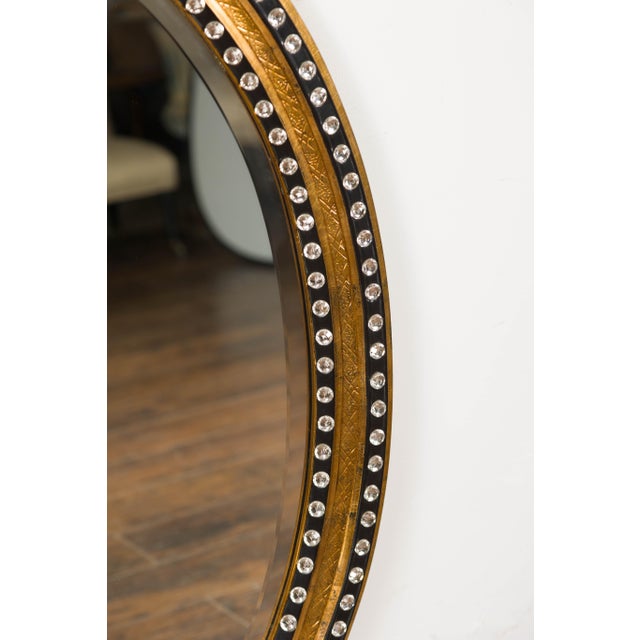 An Irish Midcentury oval shaped mirror with gilded and ebonized wood, adorned with cut glass, diamonté décor. Embodying...