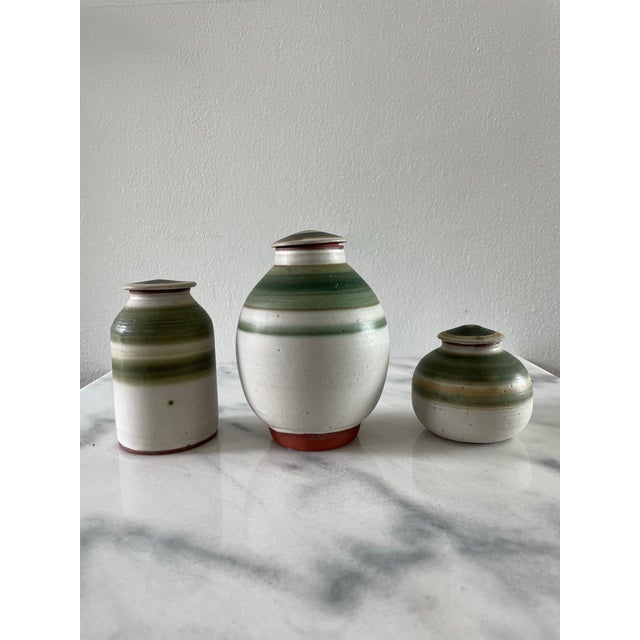 A set of three studio ceramic jars with attractive light gray and green striped glaze design. The containers have a terra...