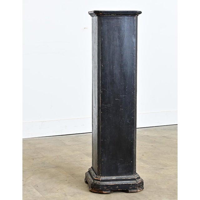 A tall vintage wooden pedestal, painted with a worn black paint finish, is perfect for displaying plants or decorative...