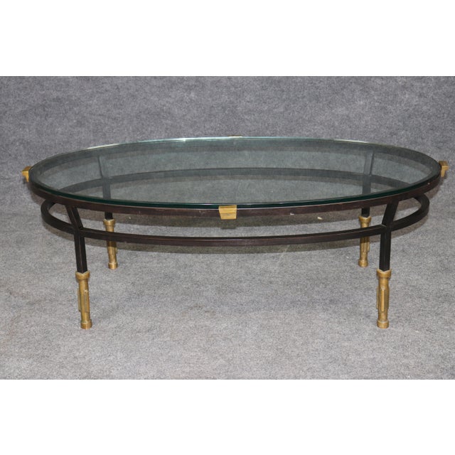 This handsome contemporary oval coffee table, combining dark-finished steel, warm brass accents, and a substantial clear...