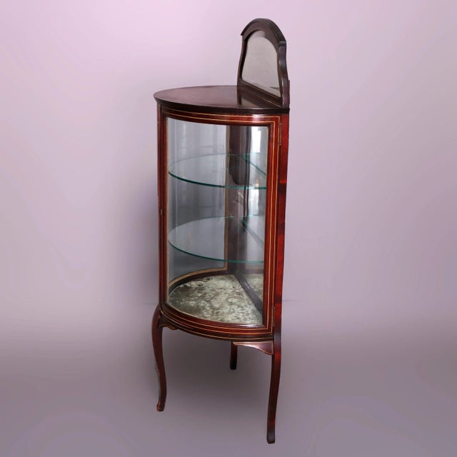 An antique French Louis XVI vitrine offers mahogany construction in demilune form having shaped and mirrored backsplash...