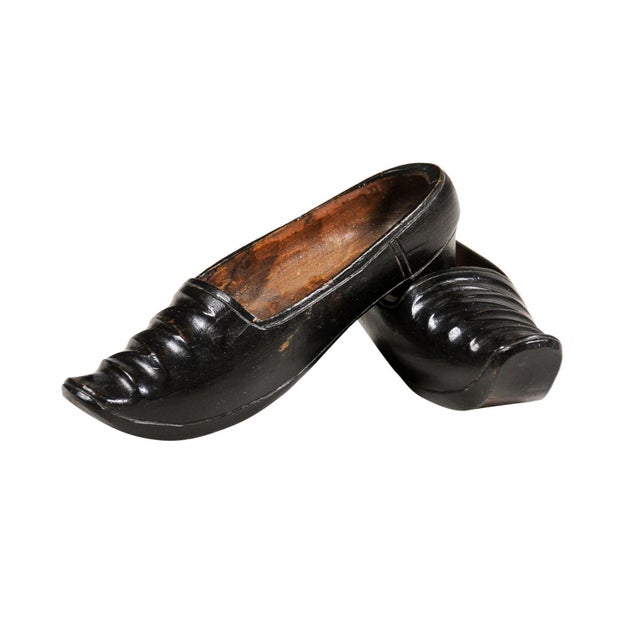 A small pair of antique Dutch carved wooden ladies' clogs from the 19th century, with black paint, square noses, wrinkled...