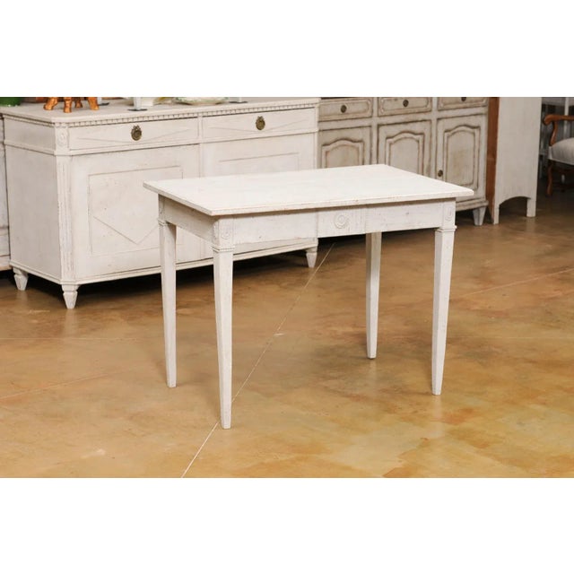 A Swedish Gustavian style painted wood table from the late 19th century, with carved rosettes and tapered legs. Created in...