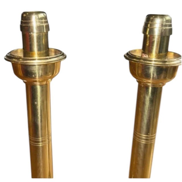 An elegant pair of vintage brass candlesticks featuring tall, slender column-form stems, stepped circular bases, and...