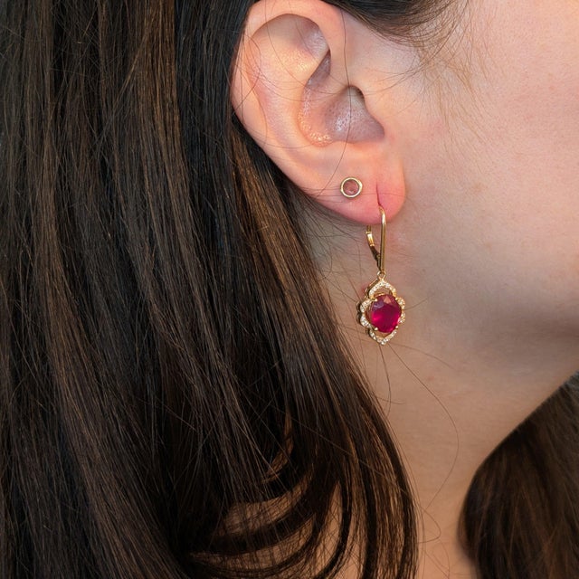Turn heads with these fiery crimson-red Ruby dangle earrings, set in solid 14K Yellow Gold. Each earring centers a hand-...