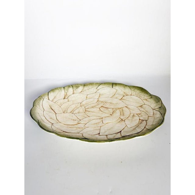 An elegant oval glazed ceramic platter, featuring a delicate, slightly raised pattern of overlapping leaves. The cream-...