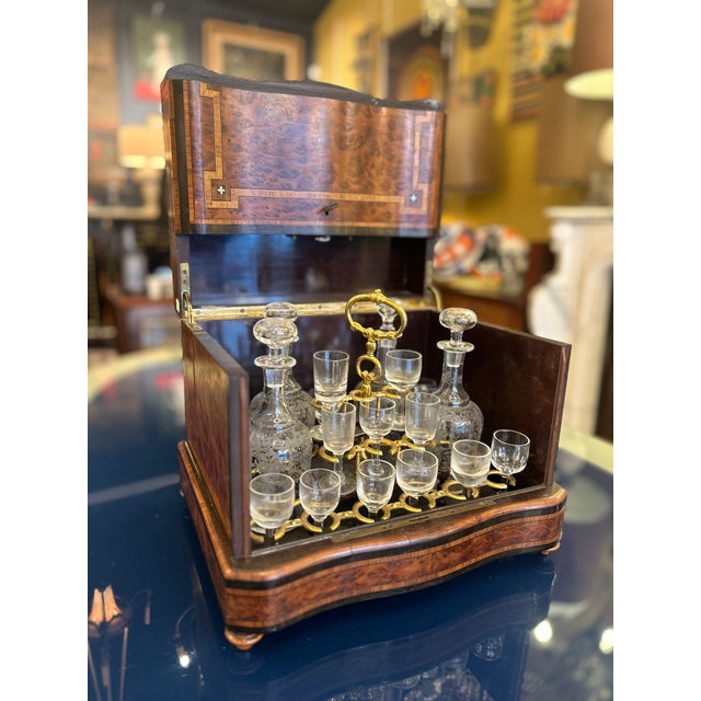 A liqueur cabinet with a drop-down lid made of burl walnut, featuring light wood marquetry bands forming a geometric...
