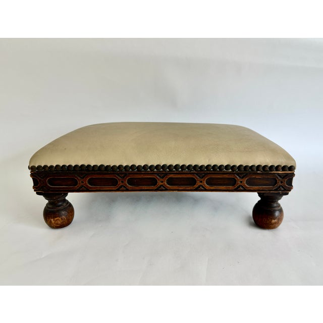 This Victorian carved oak footstool featuring a light tan leather upholstery, tight nailhead trim and bun-style feet has...