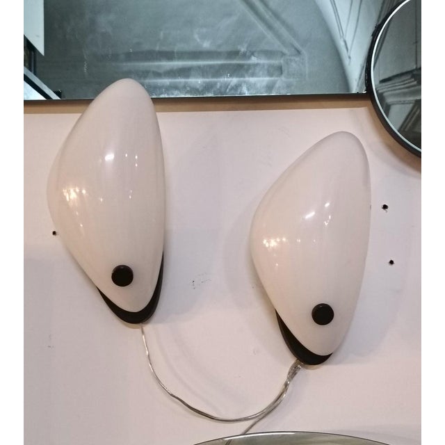 A pair of wall lamps featuring an acrylic glass shade, a black metal frame and internal brass screws. The “petal”-shaped...