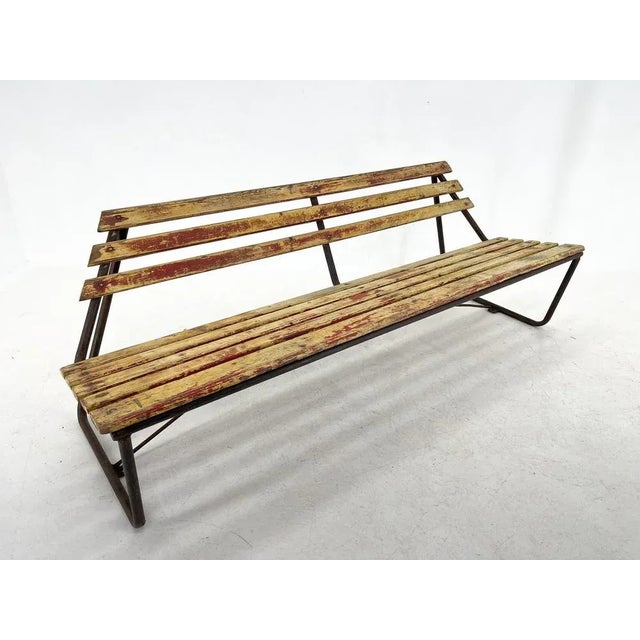 Vintage wooden bench with atypical shape. The metal construction is very stable. The wooden slats have the original paint...