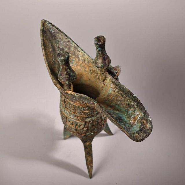 This is a Chinese archaic‑style bronze Jue, an ancient ritual wine drinking vessel. Features characteristic spout, column...
