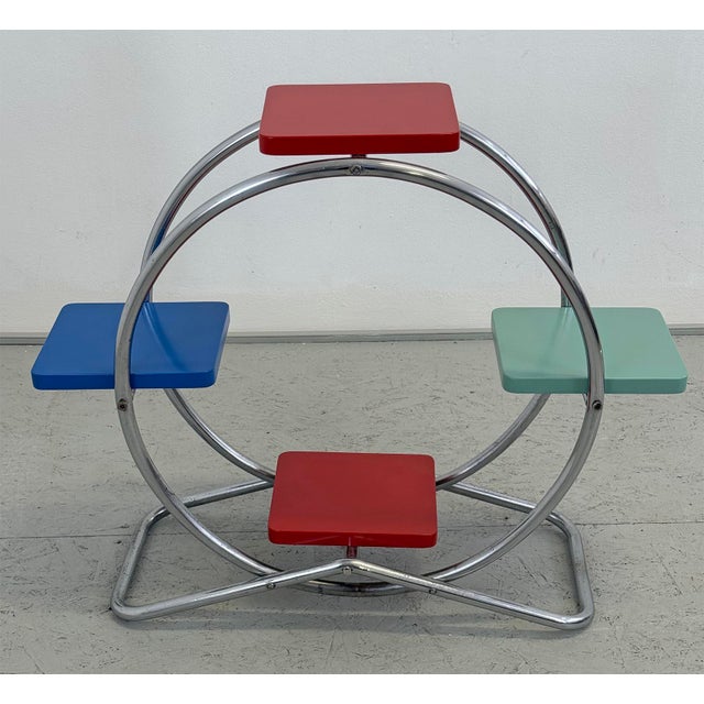 A distinctive Functionalist plant stand featuring a circular chrome-plated tubular steel frame and four colourful wooden...