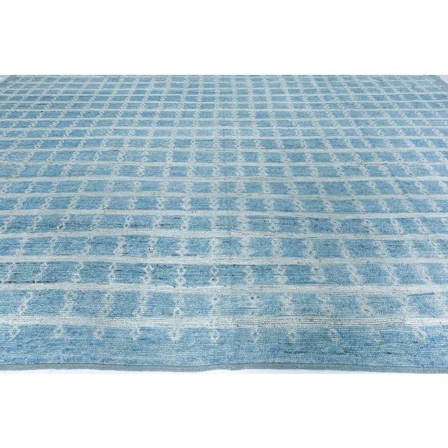 This striking modern hand-knotted wool rug features a serene palette of soft sky blues and ivory, arranged in a rhythmic,...