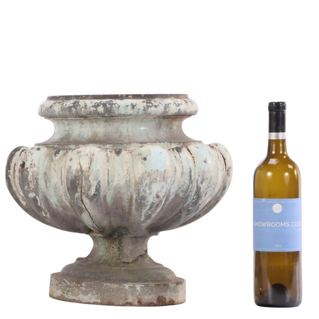 An urn displaying a handsome classical silhouette with a rounded gadrooned body resting on a round plinth base and capped...