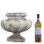 An urn displaying a handsome classical silhouette with a rounded gadrooned body resting on a round plinth base and capped...