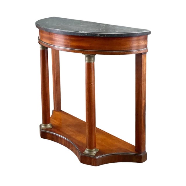 A gorgeous French Empire style demilune console table in mahogany with finely cast bronze mountings and black marble top....