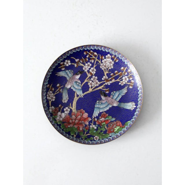 A vintage cloisonné enamel plate in deep cobalt blue with gold trim and intricate detailing. features a finely rendered...
