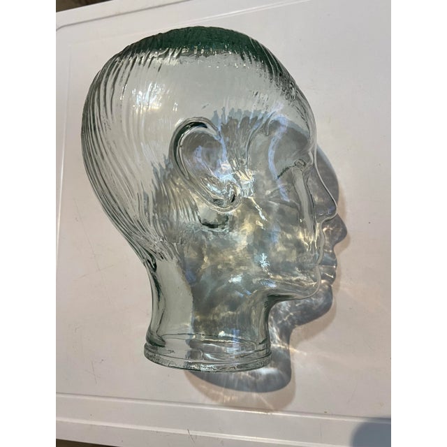 Vintage whimsical clear glass with a green tint. Lot of detail glass mannequin head. Stands 8” tall. Base opening is 4” in...