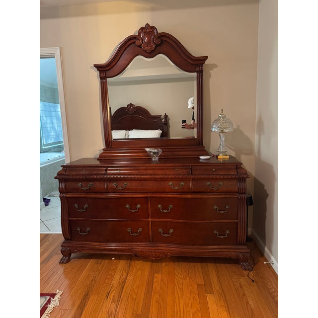 A traditional cherry-finish triple dresser with its attached arched mirror, from a four-piece carved bedroom suite. Seven...