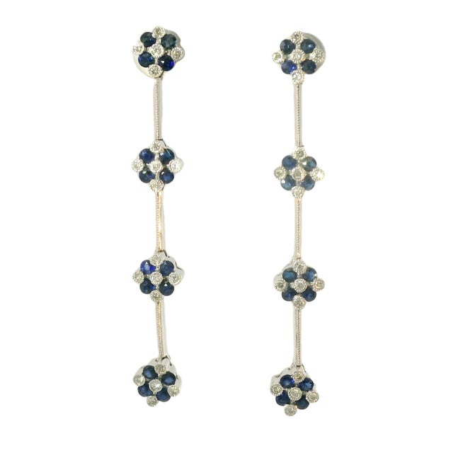 Elegant 14K white gold chandelier earrings featuring sparkling diamonds and deep blue sapphires in a delicate floral tier...