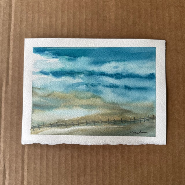 A serene watercolor painting capturing the essence of a coastal landscape. Soft blues and sandy tones blend effortlessly...