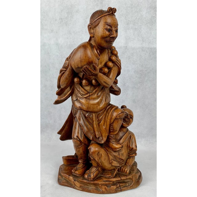 The Chinese carving of a male water bearer with a boy at his feet. The carved teak figure has a rectangular cartouche on...
