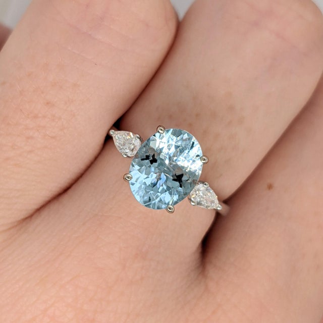 A sky blue aquamarine sits in a clear sea-blue at the heart of this solid 14K white gold ring, flanked by fifty-eight...