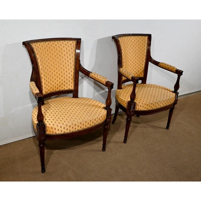 Solid mahogany armchairs resting on front feet turned in a spindle and saber rear feet. The continuity of the front feet,...