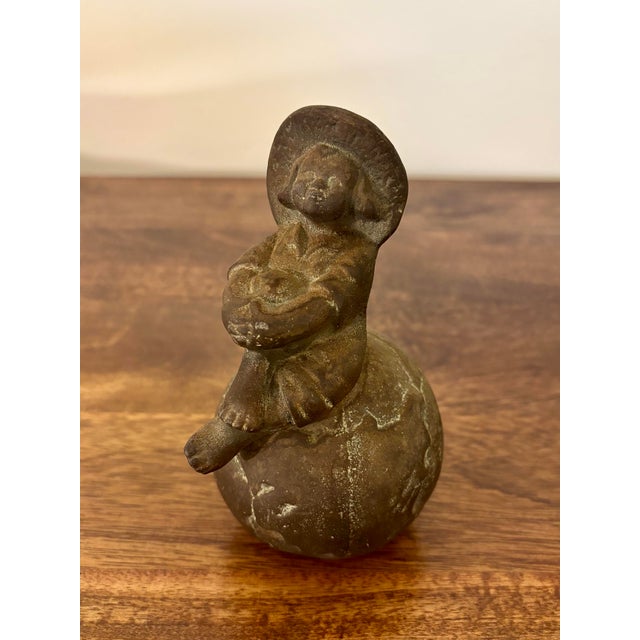 A charming early 20th-century bronze figure of a young boy seated atop a globe, rendered with warmth, detail, and a...