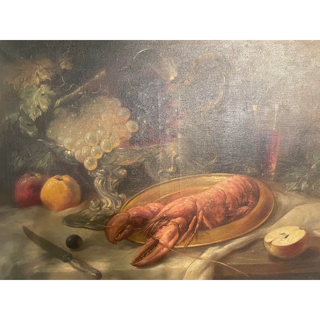 Signed still life oil painting depicting a lobster on a platter, flanked by fruits, a knife, a glass, and an ornate silver...