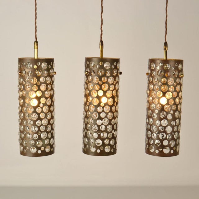 Set of three elongated blown glass pendants encased in brass cones perforated with holes of varying sizes. The hot and...