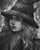 In "Divination," a figure adorned with a wide-brimmed hat and flowing hair gazes thoughtfully, capturing a moment of...