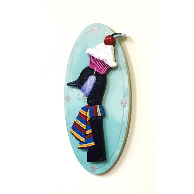 This artwork features a whimsical depiction of a bird adorned with a colorful striped scarf and a playful cupcake hat,...