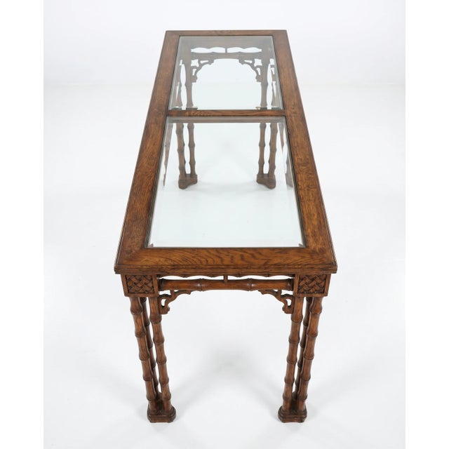 Beautifully detailed faux-bamboo console table featuring carved lattice corner blocks, decorative fretwork, and a glass-...