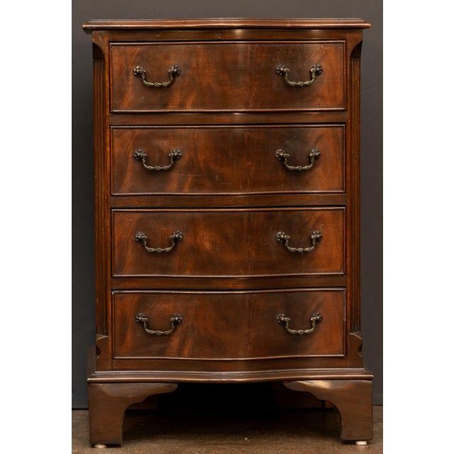 A fine English small chest of drawers or commode of patinated flame mahogany, featuring a moulded serpentine top over a...