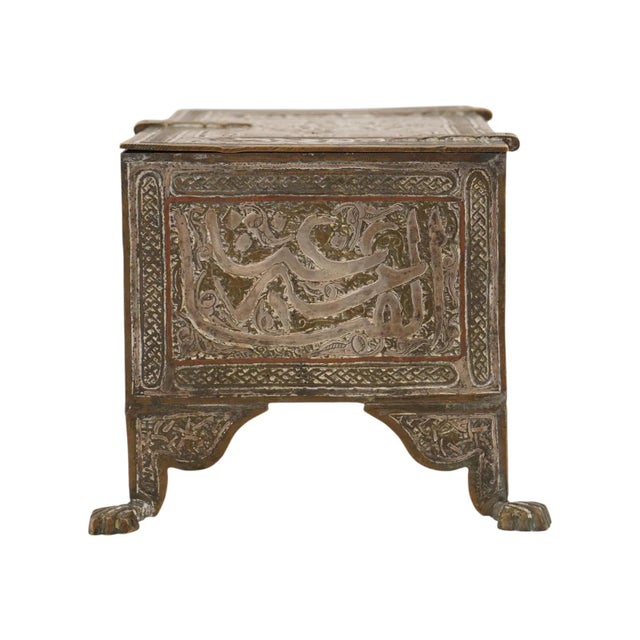 An antique box in the Syrian or Mamluk style, crafted from brass with intricate silver inlay, featuring a rectangular form...