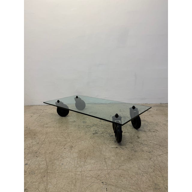 Designed by Gae Aulenti, this low coffee table consists of a tempered glass top supported by four black industrial wheels...