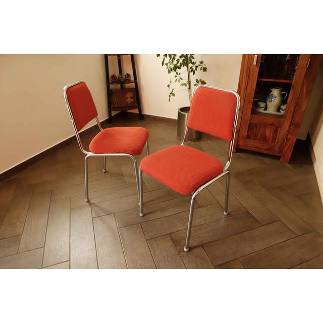 Pair of retro chairs from the 1970s featuring tubular chrome frames and vibrant red upholstered seats and backrests. The...